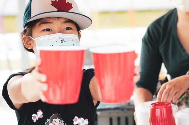 Samantha: Girl holding out two red cups during a lemonade stand fundraising event