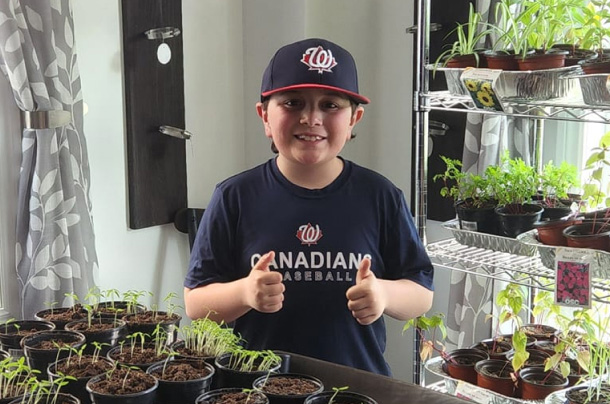 Tanner: Boy posing in front of many potted plants that will be sold to raise money for charity